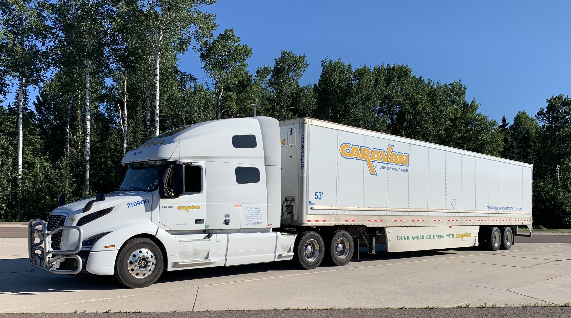 White Caravan reefer trailer side profile against treeline