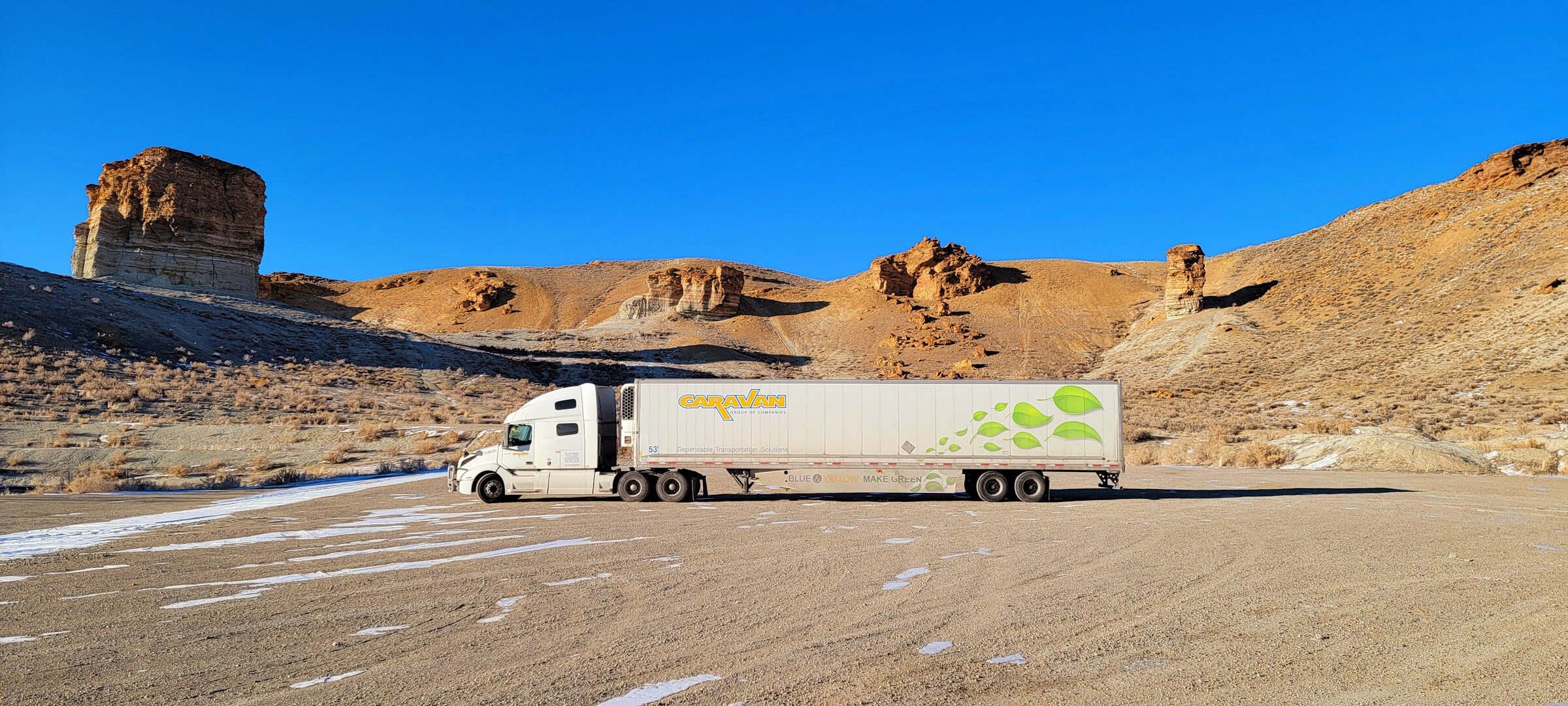 Caravan reefer trailer side profile beside a sandstone butte under deep blue sky