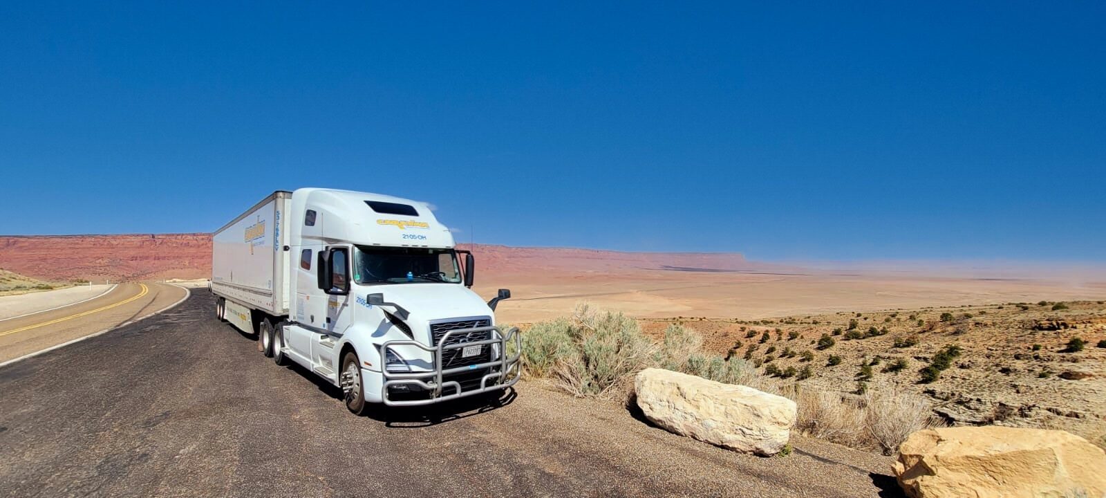 Caravan rig on open desert highway with sweeping red-rock vista