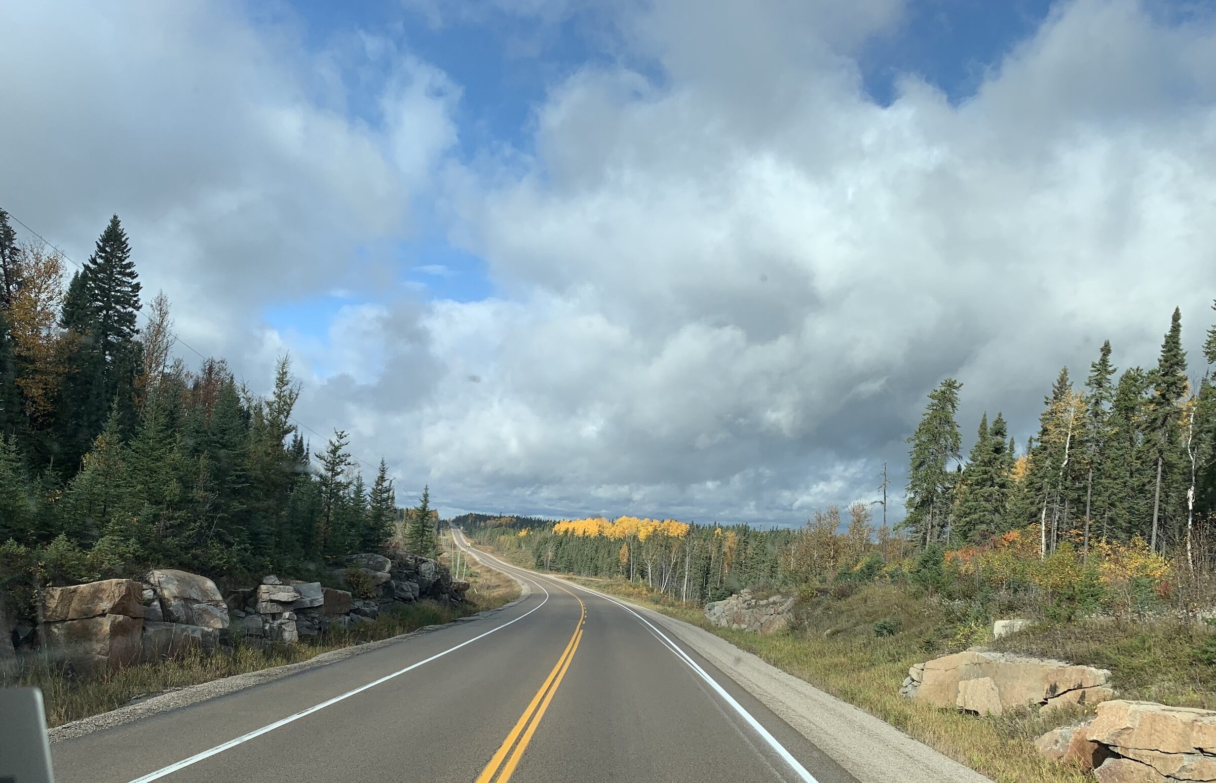 Autumn Canadian highway curving past golden trees under dramatic broken clouds